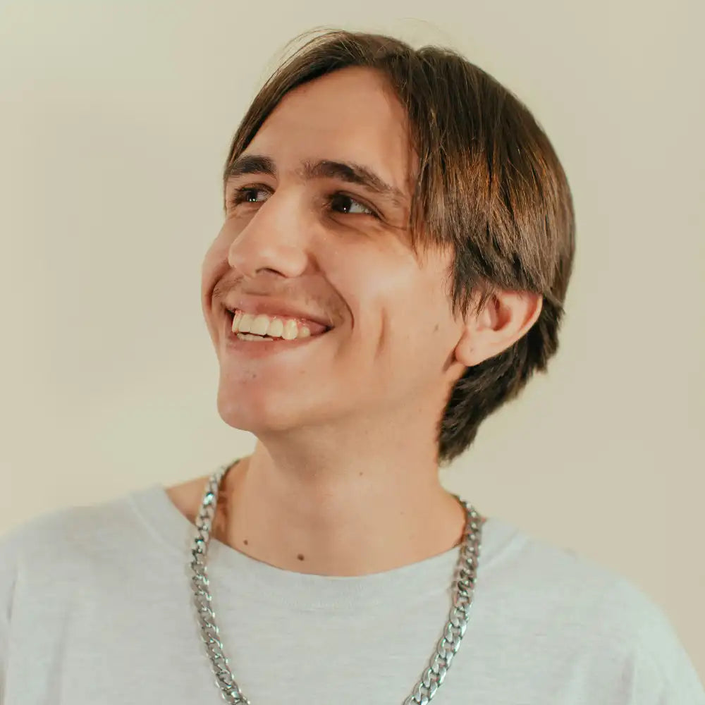 Person wearing a light gray shirt and a chain necklace against a plain background
