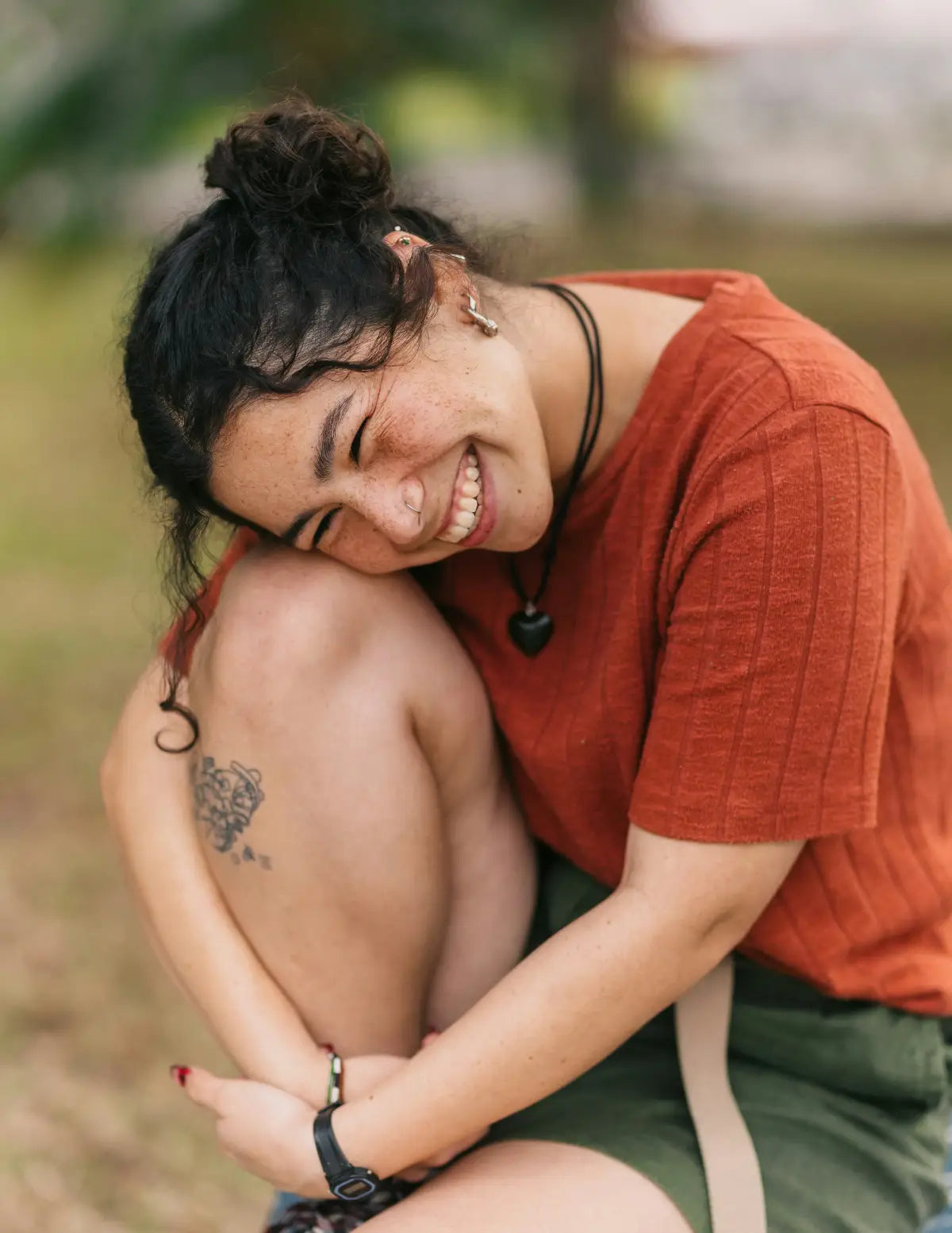 Person sitting outdoors with a tattoo on their arm, wearing an orange shirt and green shorts. Image credit: Jordan Gonzales