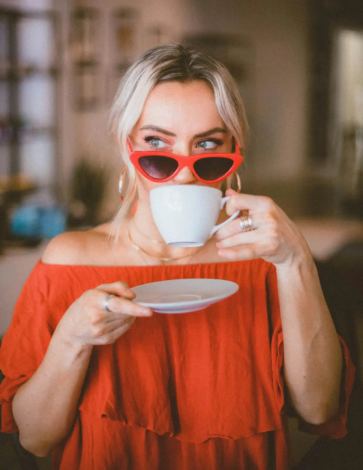 Woman in a red dress and sunglasses holding a white mug and saucer.