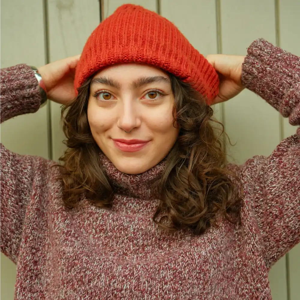 Person wearing a red knit beanie and matching sweater against a neutral background