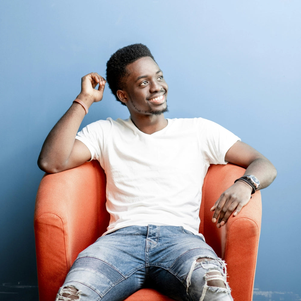 Man in white shirt and jeans sitting in orange chair with blue background. Photo credit: Getty images