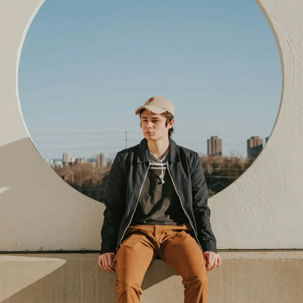Person sitting outdoors with a circular concrete structure and city skyline in the background - image by Rayul