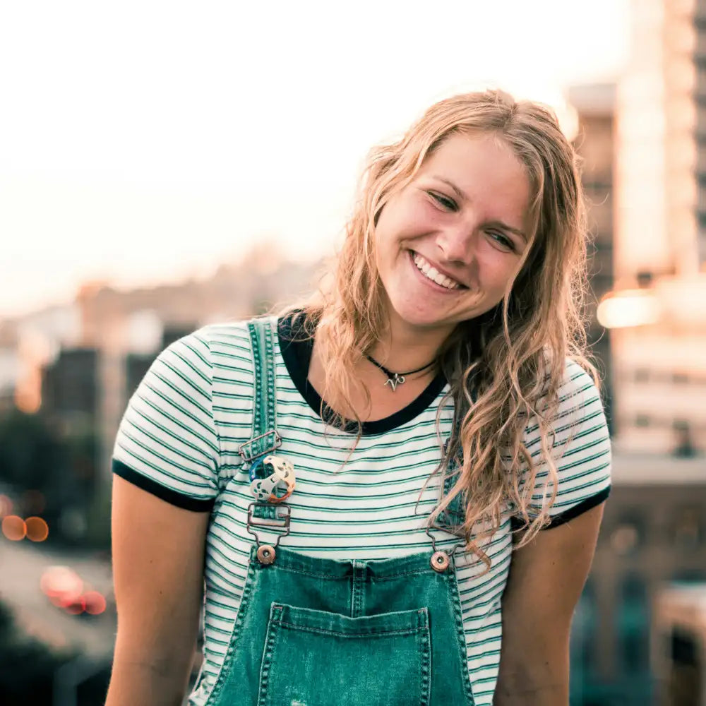 Woman wearing a striped shirt and green overalls with a blurred cityscape background. Photo credit: Ben Dutton