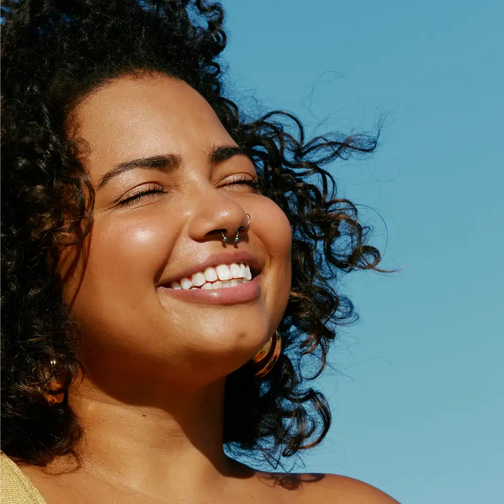 Woman with a nose ring smiling against a clear blue sky. Photo credit: Natalia Blauth