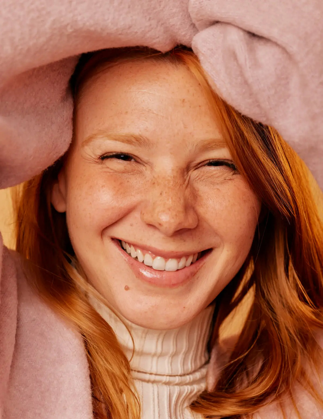 Happy young woman wearing a pink sweater with arms over head. Photo credit: Natalia Blauth