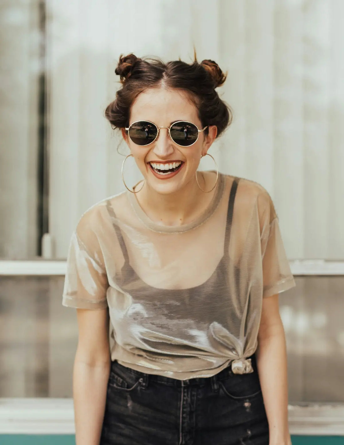 Woman wearing sunglasses and a sheer top with dark jeans indoors. Image credit: Brooke Cagle